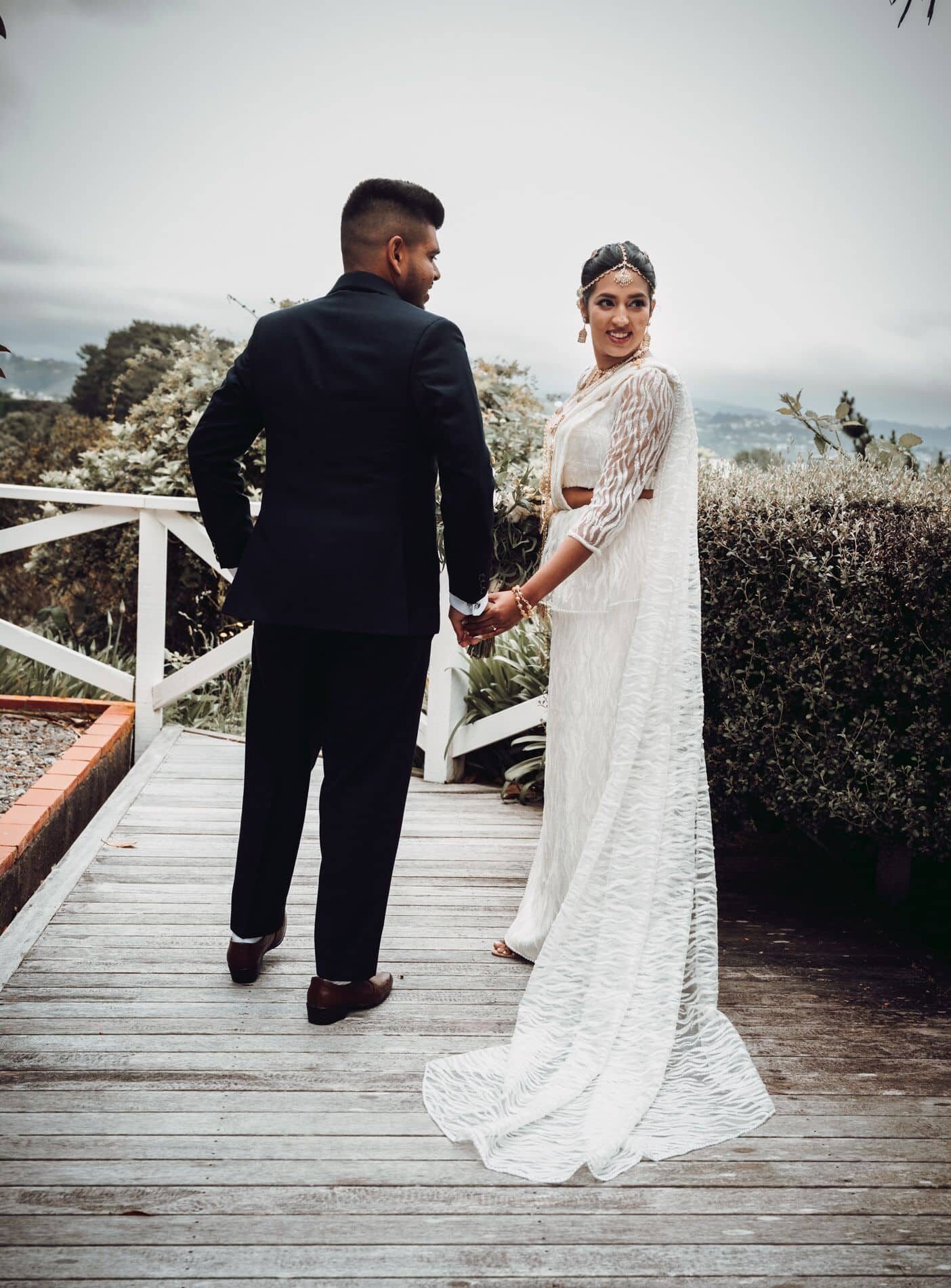 A newlywed couple shares a romantic moment at The Lodge, Pauatahanui Inlet, as they walk hand in hand with stunning natural scenery in the background