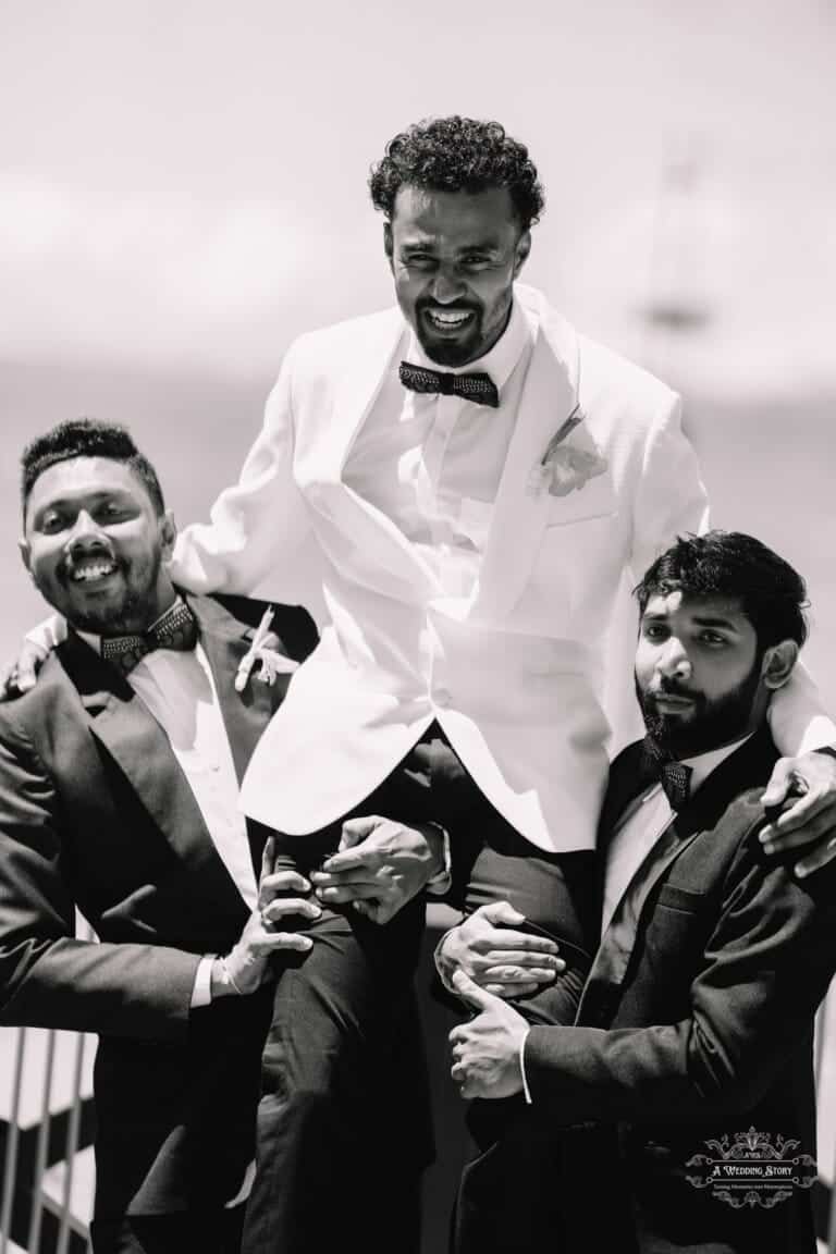 A black and white photo capturing a joyful moment as the groom is lifted by his groomsmen during a waterfront wedding in Wellington