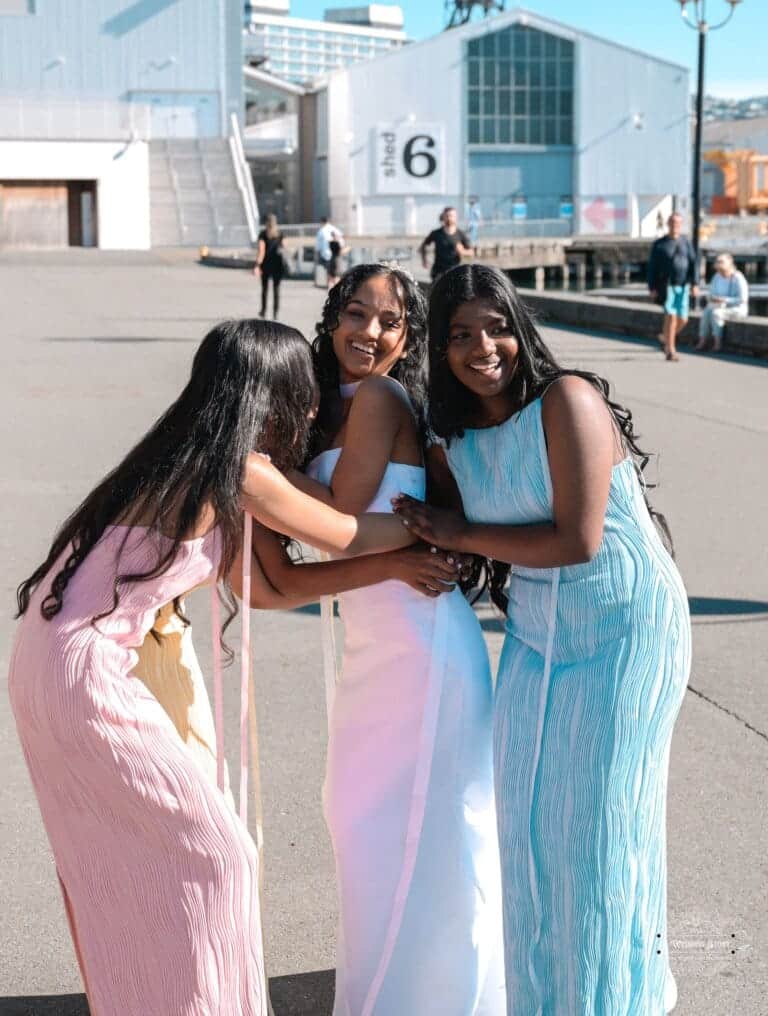 A bride in a white gown embraces her bridesmaids in pastel dresses, laughing together at Wellington waterfront