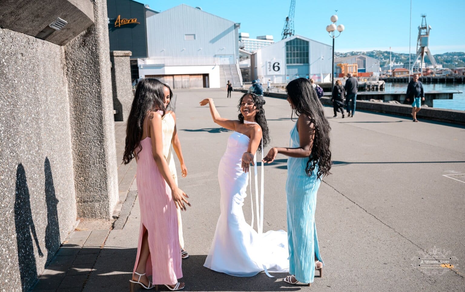 A bride in a white gown shares a joyful moment with her bridesmaids in pastel dresses at Wellington waterfront