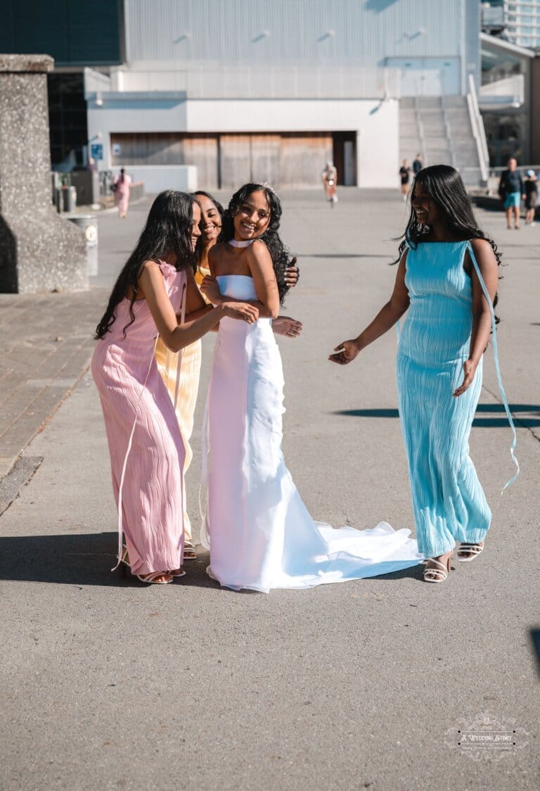 A joyful bride in a white gown shares a fun moment with her bridesmaids in pastel dresses at Wellington waterfront