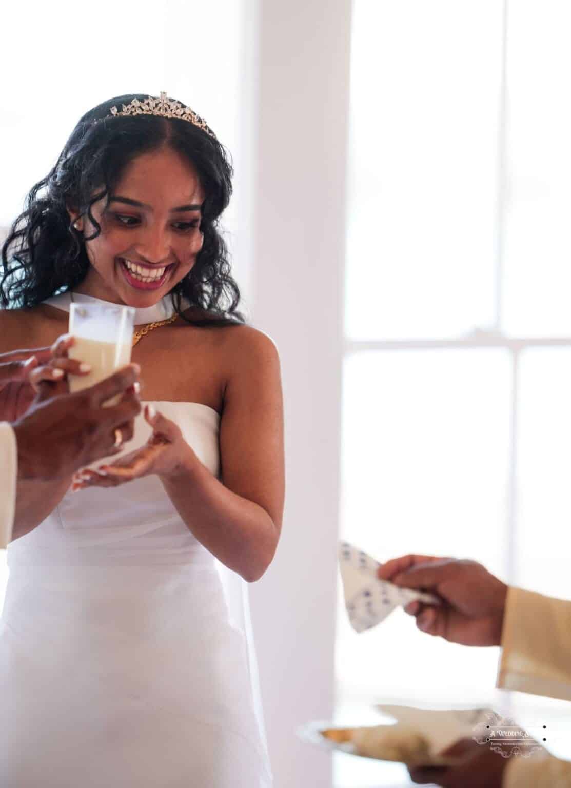 A radiant bride in a white gown and tiara smiles while receiving a ceremonial drink at her wedding in Wellington