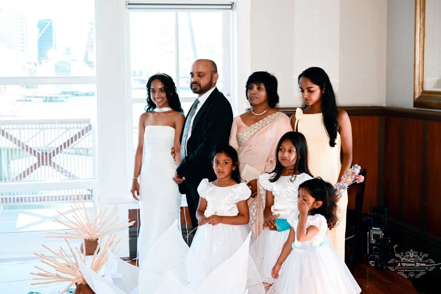 The bride poses with her family at a wedding in Wellington, surrounded by elegantly dressed relatives and flower girls in a beautifully lit venue