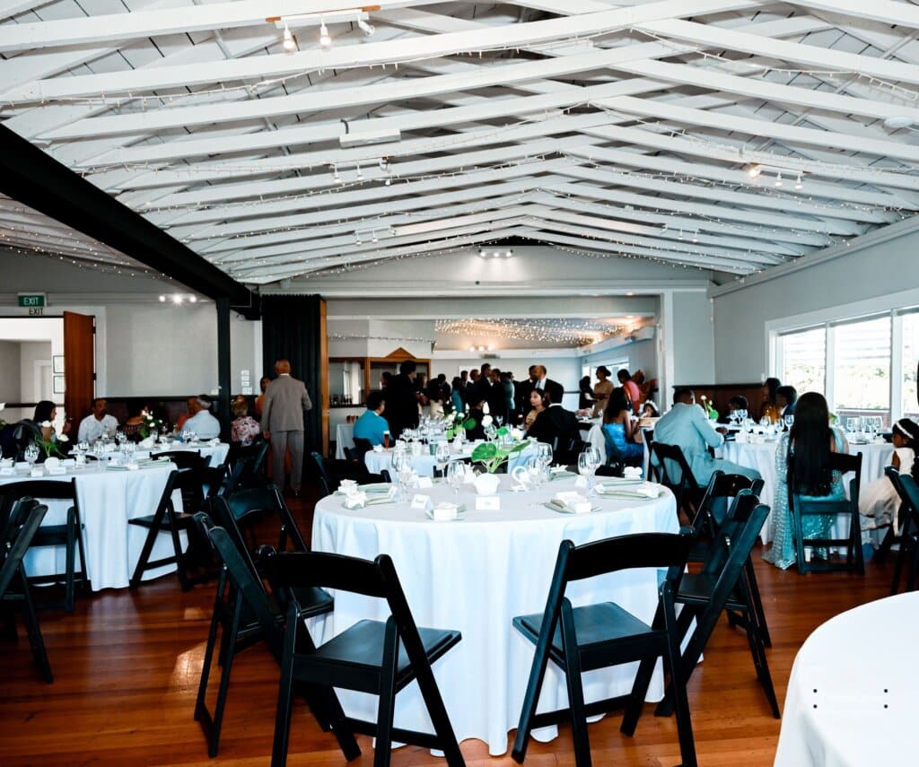 A beautifully decorated wedding reception venue in Wellington, featuring round tables with white tablecloths, floral centerpieces, and a lively gathering of guests