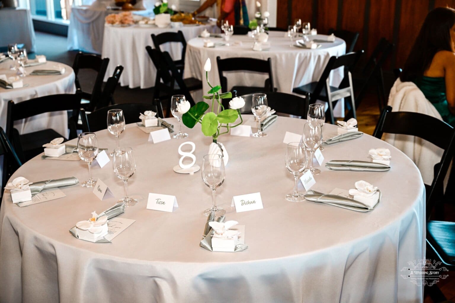 A beautifully arranged wedding reception table with white table linens, green floral centerpieces, name cards, and elegant tableware in Wellington