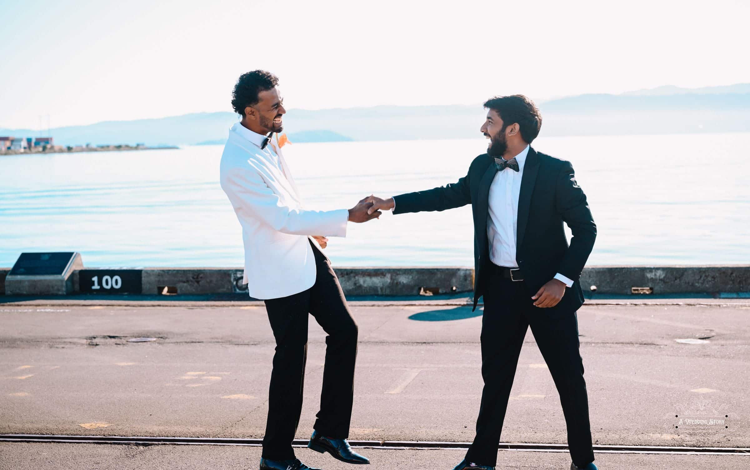 Groom and best man sharing a joyful moment at Wellington Waterfront during a wedding celebration