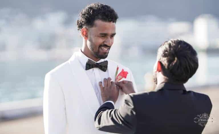 A groom smiles as his best man carefully adjusts his boutonniere on his wedding day