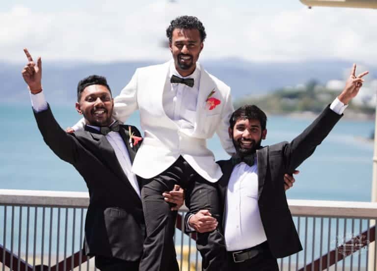 The groom is lifted by his groomsmen, celebrating joyfully at Wellington Waterfront with the ocean in the background