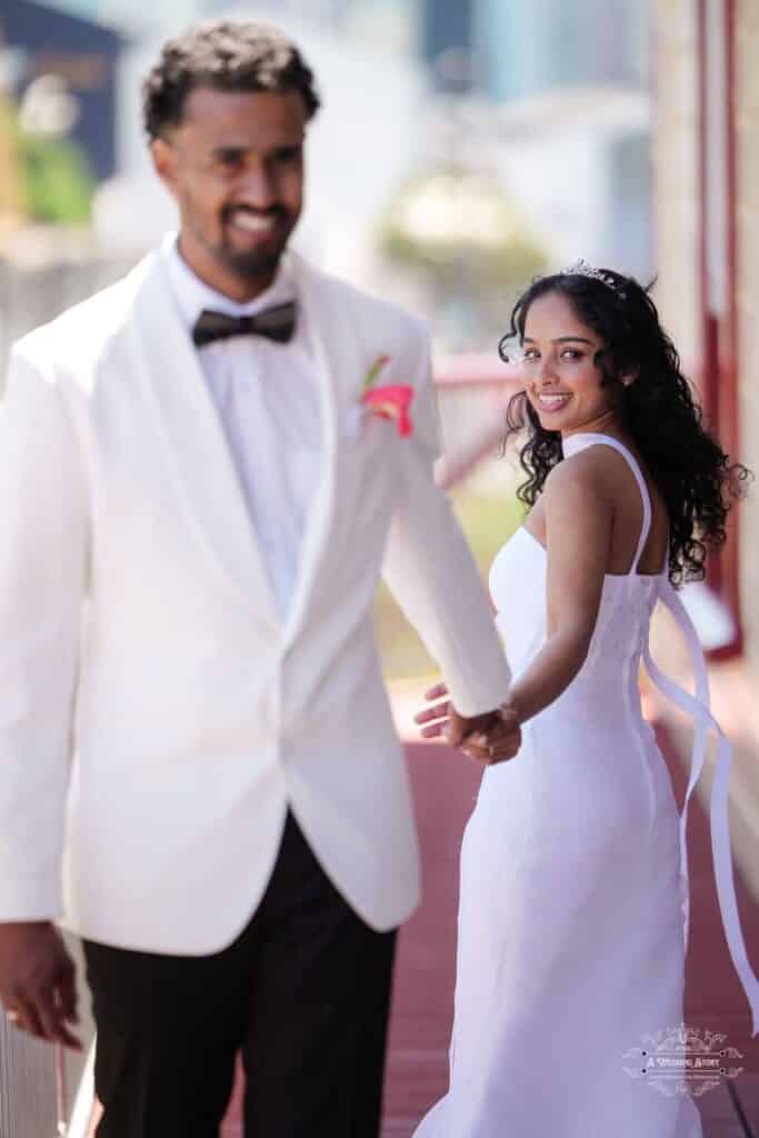 A joyful bride looks back with a radiant smile as she holds hands with her groom, capturing a romantic wedding moment