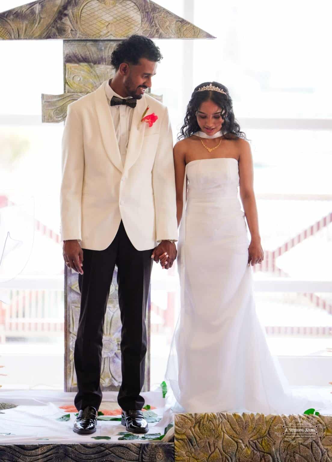 A newlywed couple dressed in elegant wedding attire holds hands during their traditional wedding blessings ceremony in Wellington, New Zealand