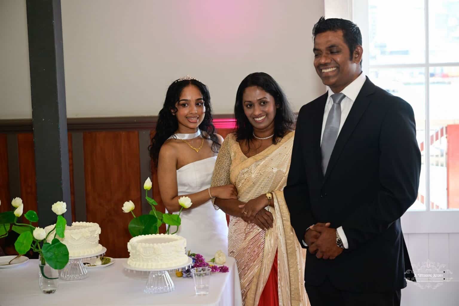 A bride in a white gown poses with family members during a wedding celebration in Wellington, standing beside a beautifully decorated cake table