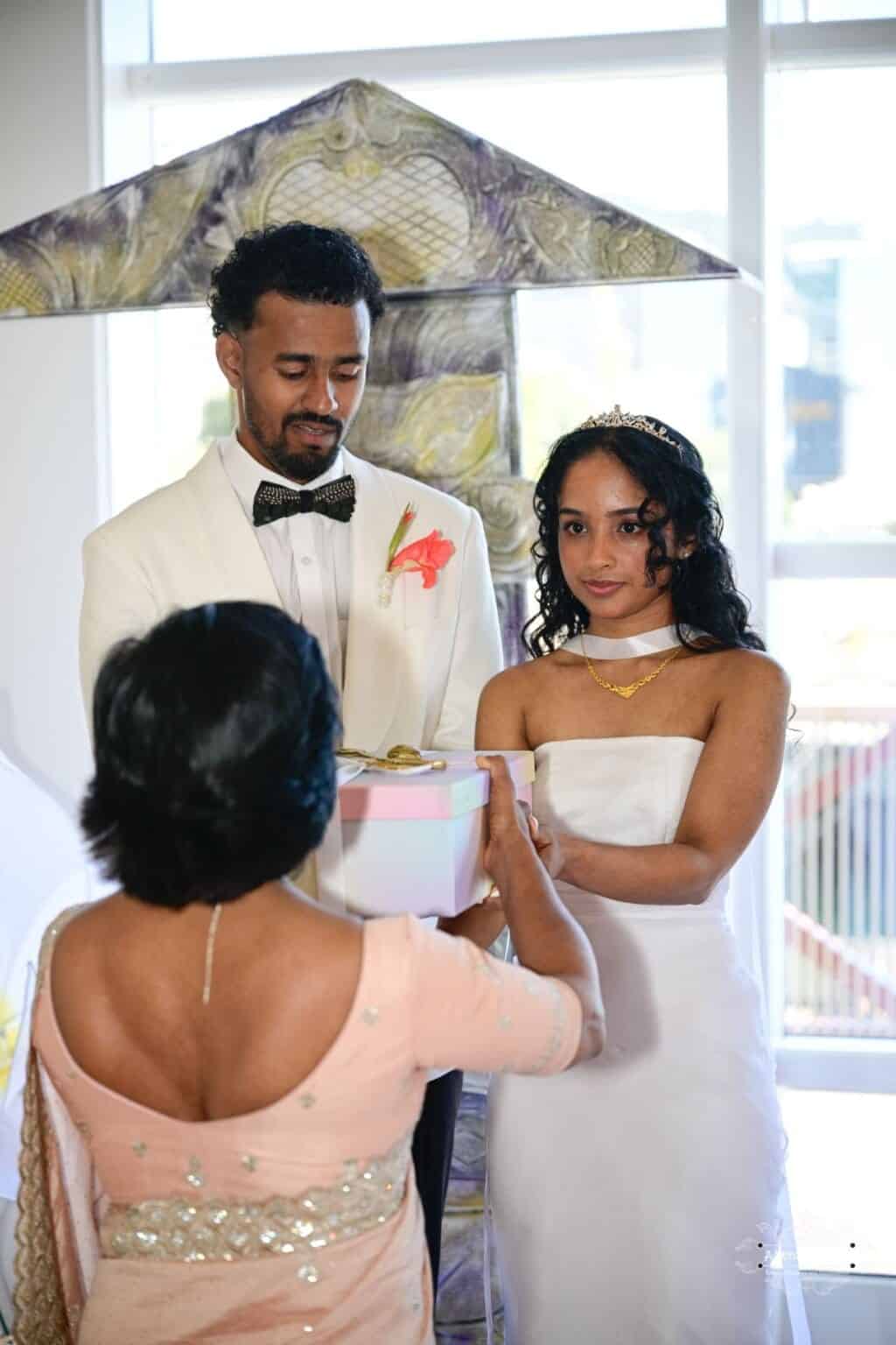 A bride and groom receive a beautifully wrapped wedding gift from a family elder during a cultural wedding ceremony in Wellington