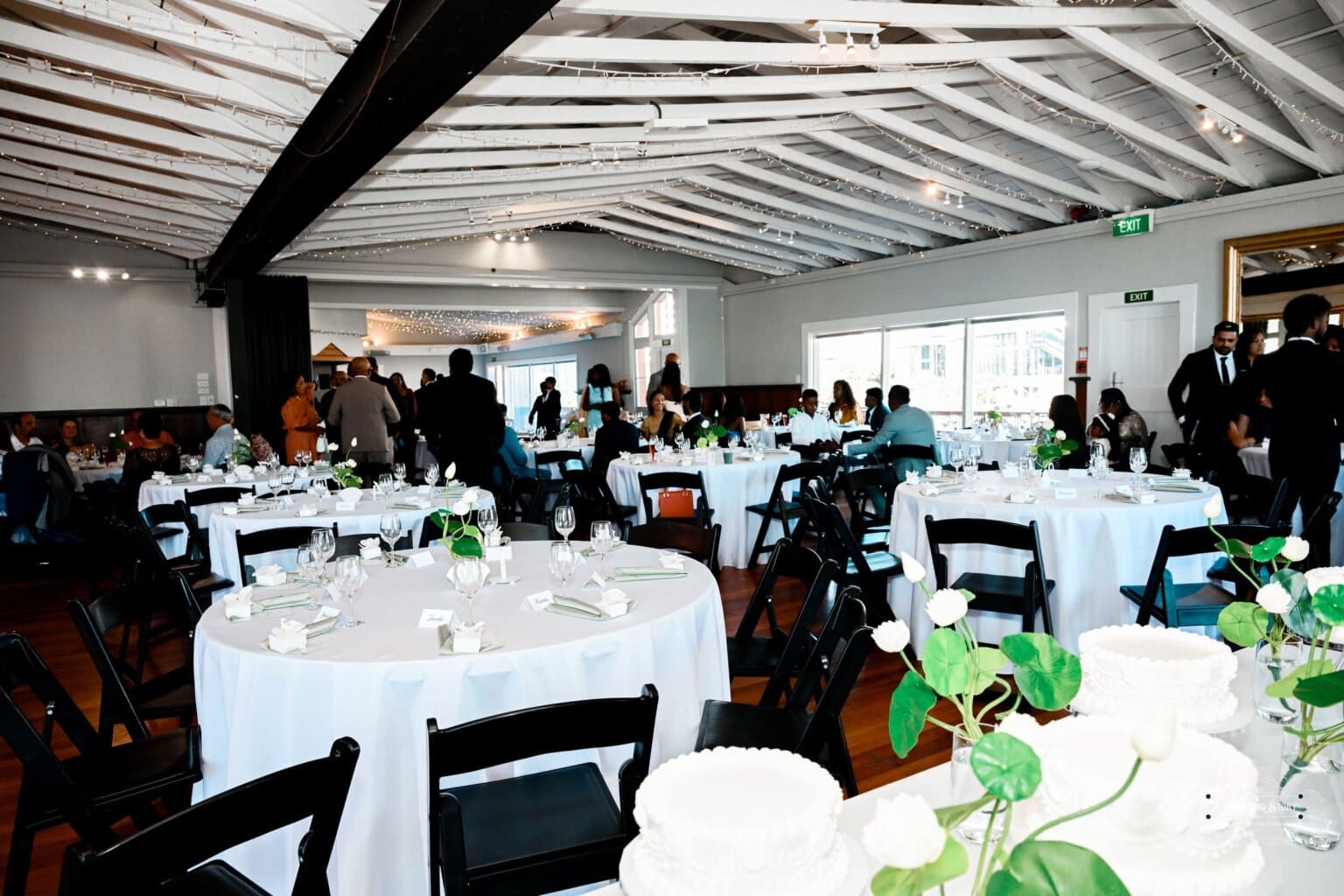 A beautifully decorated wedding venue in Wellington with white table settings, black chairs, and floral centerpieces, offering a scenic waterfront view