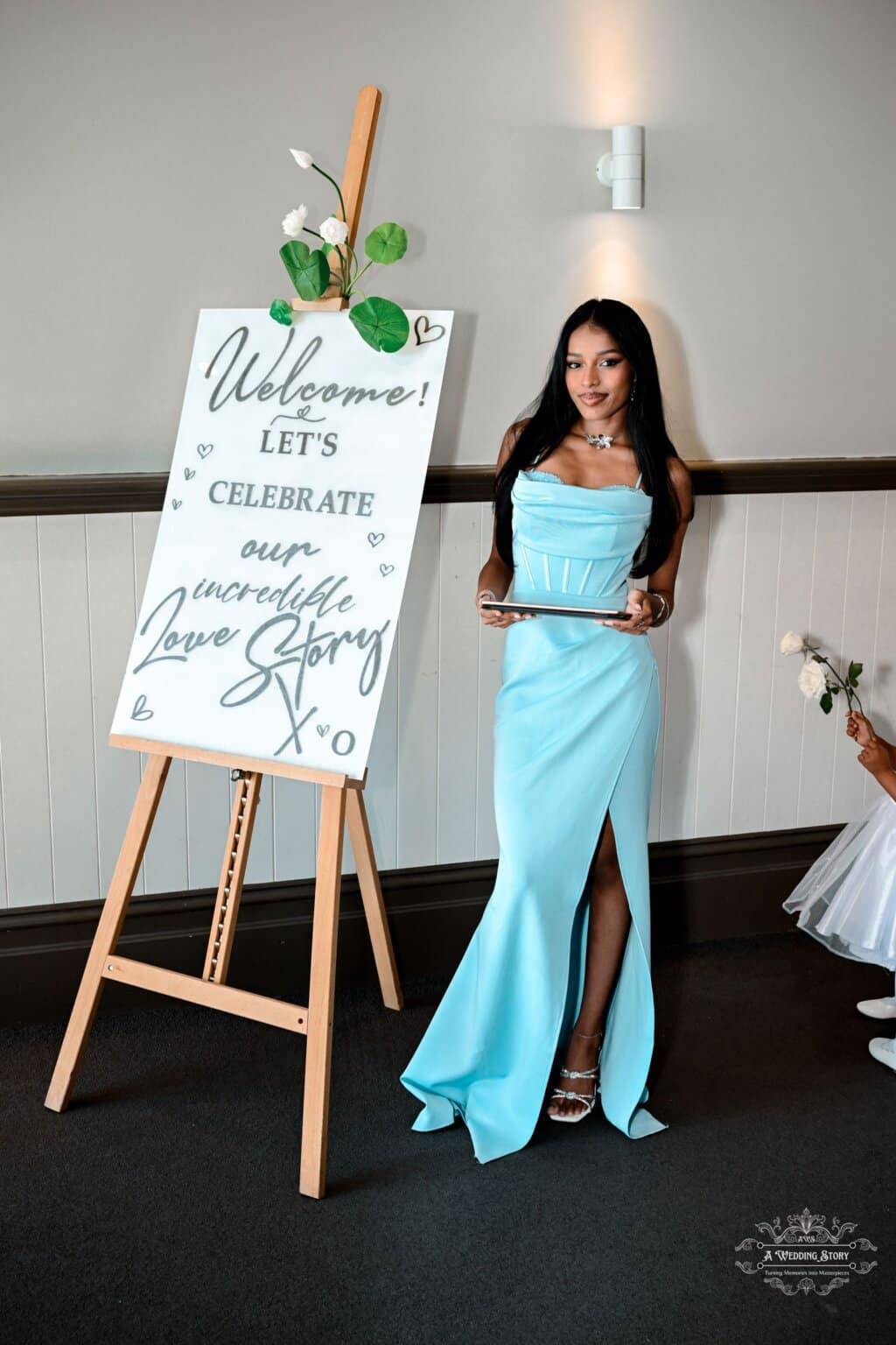 A bridesmaid in a stunning blue gown stands beside a beautifully decorated wedding welcome sign at a Wellington wedding